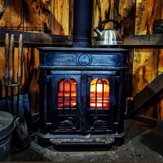 The wood stove inside the sugar shack, firebox glowing, with a steel kettle warming on top