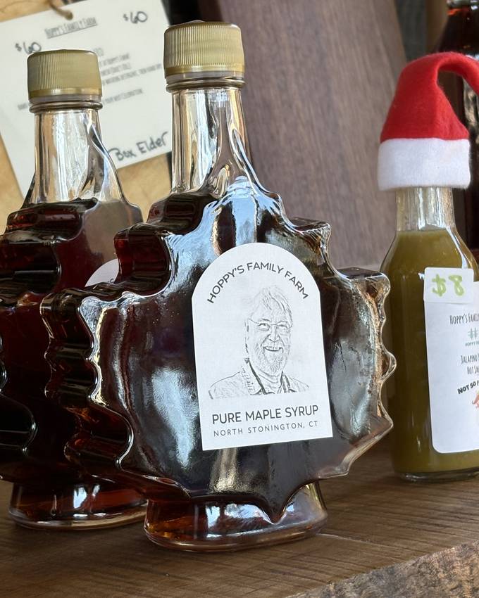 Maple-leaf-shaped glass bottles of Hoppy's Family Farm pure maple syrup on the shop shelf, one small bottle wearing a tiny Santa hat