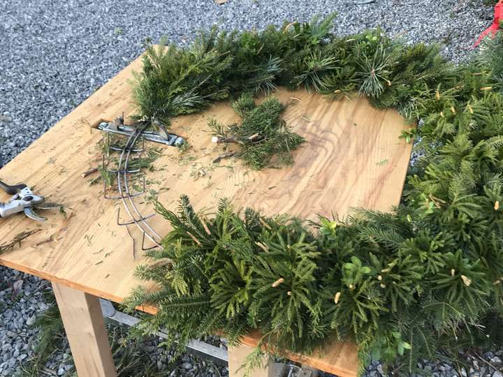 A wreath taking shape on the outdoor workbench, evergreen boughs wired by hand onto the ring